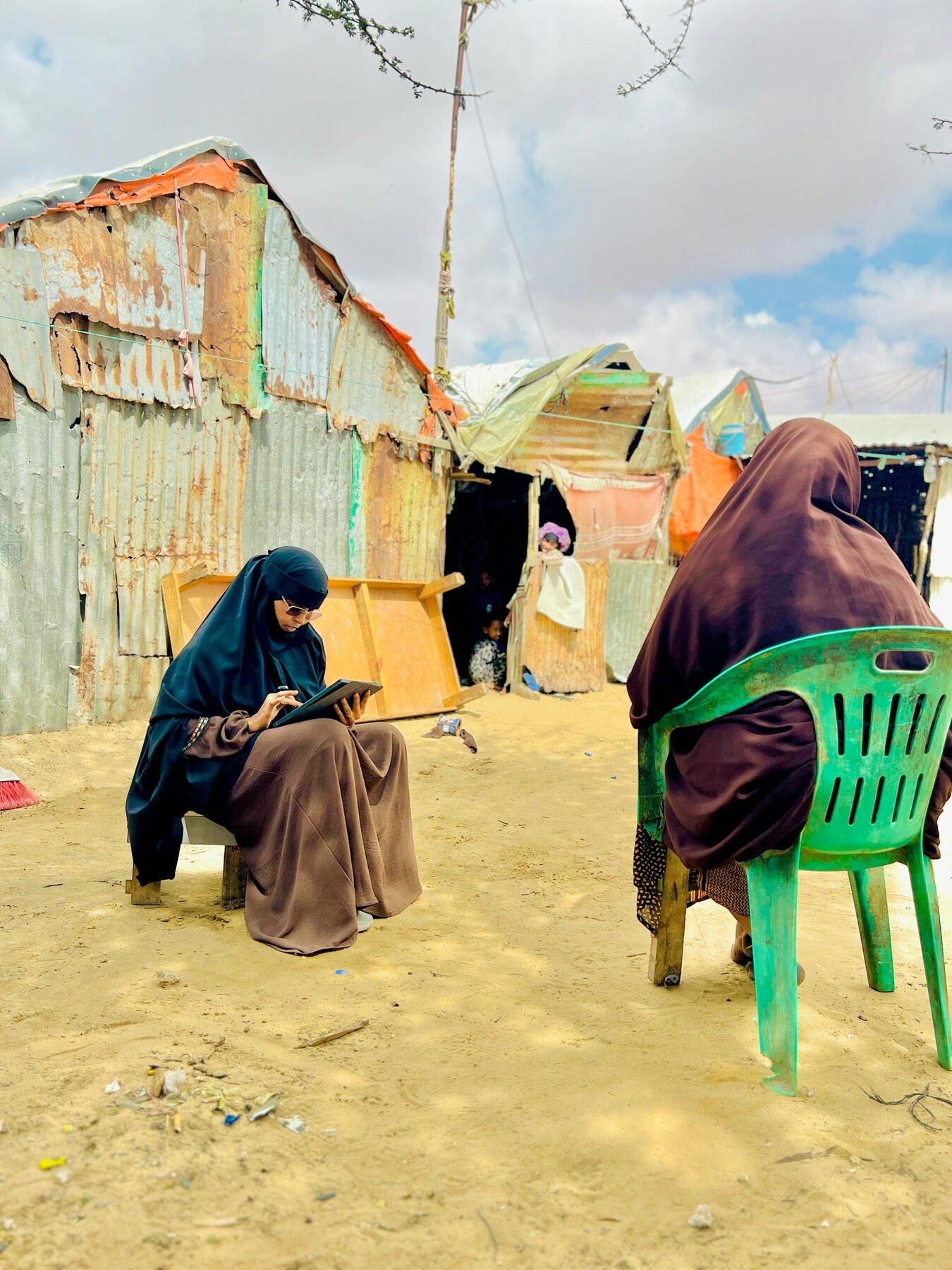 Field researcher collecting household data on a tablet outside a shelter